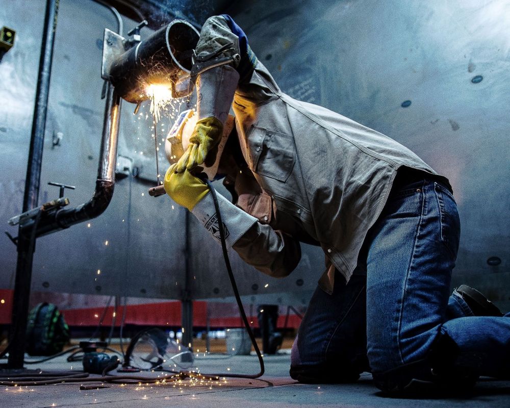 Welder kneeling at a pipe joint during the WWA welding competition